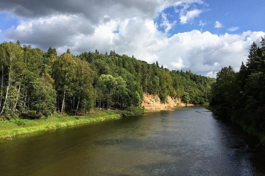 Een rivier omgeven door dicht bos, een heldere lucht en een heuvel in de verte. 1