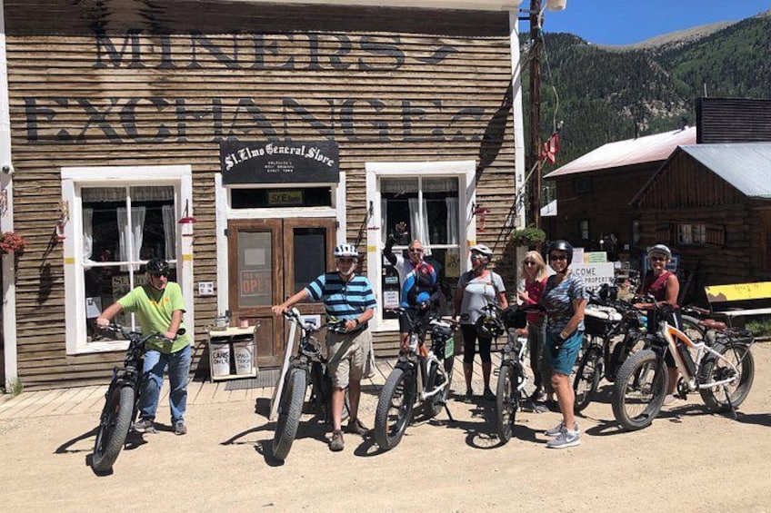Un gruppo di ciclisti di fronte a un edificio in legno con un cartello che riporta la scritta 'MINER'S EXCHANGE'. 2
