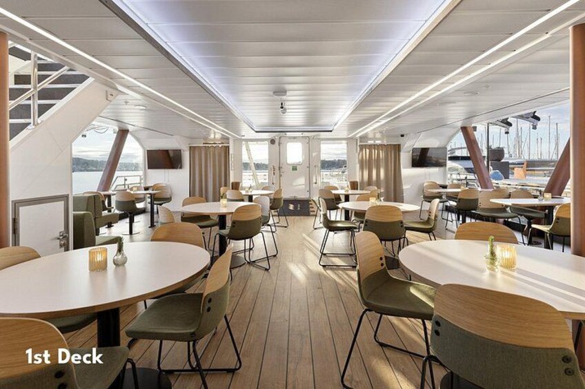 Spisested på et skib med runde borde og stole, store vinduer og udsigt til havet. 3