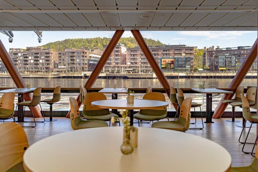 An outdoor dining area with round tables and chairs, overlooking a waterfront with buildings in the background. 4