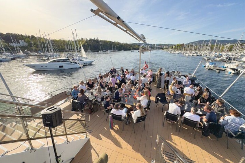 A boat deck with people dining, surrounded by calm water and sailboats. 2