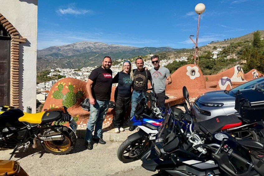 Four people standing in front of a row of motorcycles, with a mountainous landscape in the background. 4