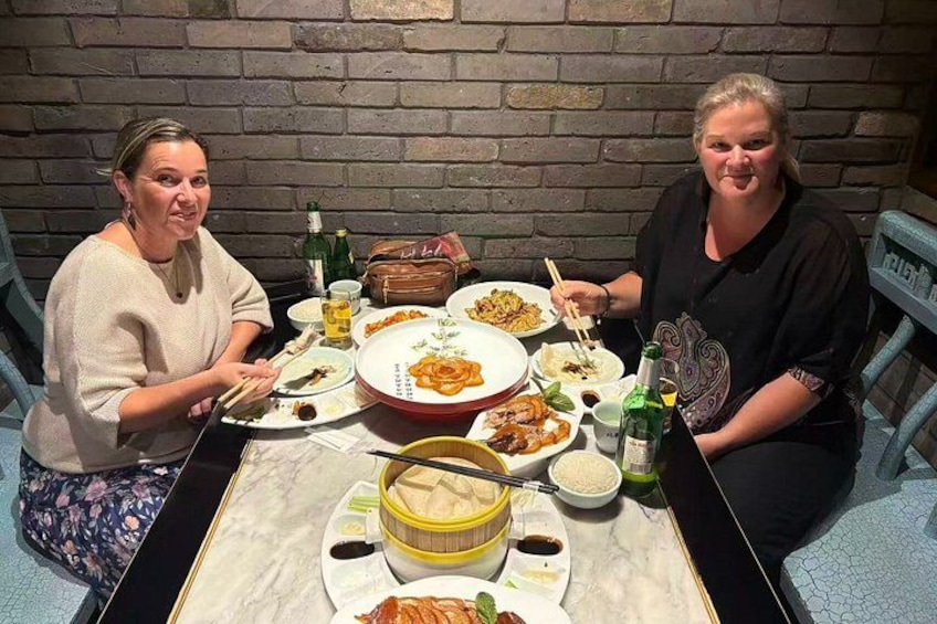Two people sitting at a table with various dishes and drinks. 1