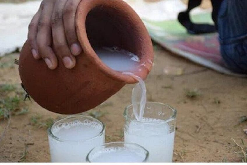 A hand pouring liquid from a clay pot into a glass. 1