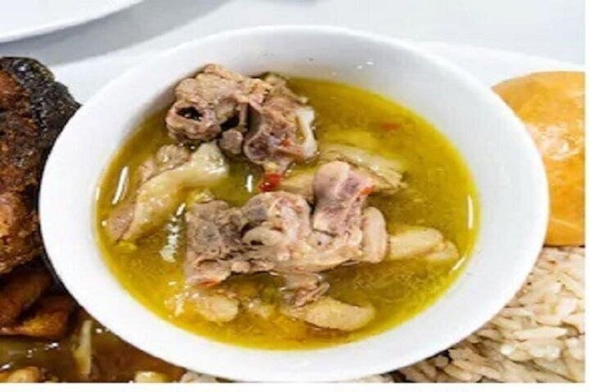 A bowl of soup with meat and vegetables, a piece of grilled meat, and a bread roll. 4