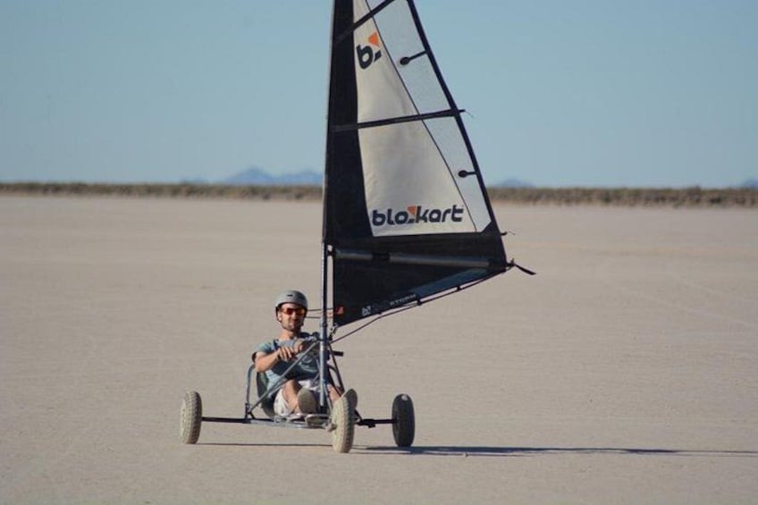 A person in a cart with a sail, driving on a flat, barren landscape. 4