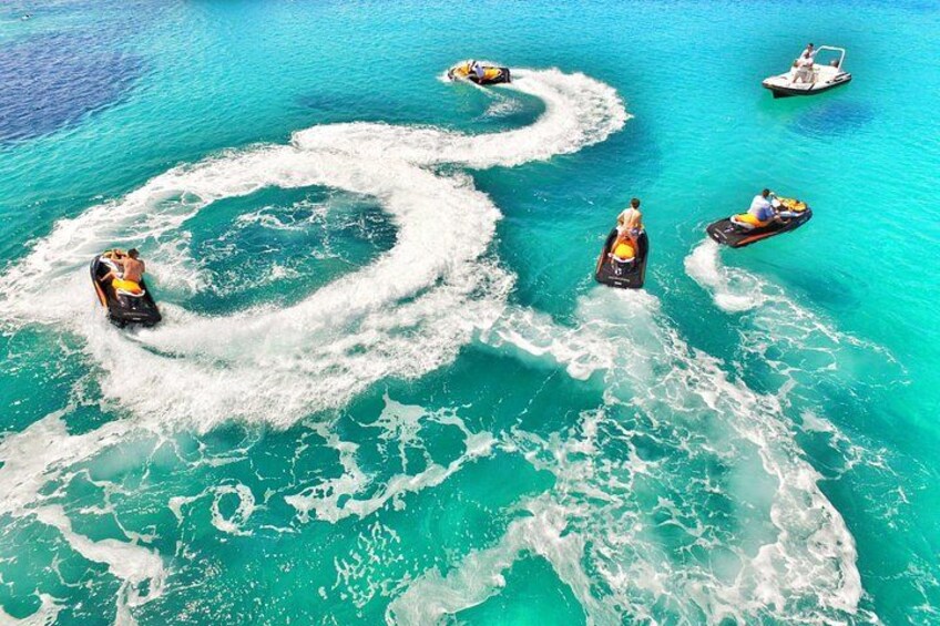 A person riding a jet ski in turquoise water, surrounded by other jet skis creating circular patterns. 1
