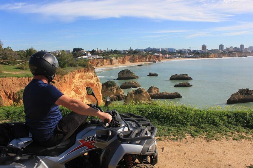 A person on a quad bike overlooking a coastal landscape with cliffs and a city in the distance. 1