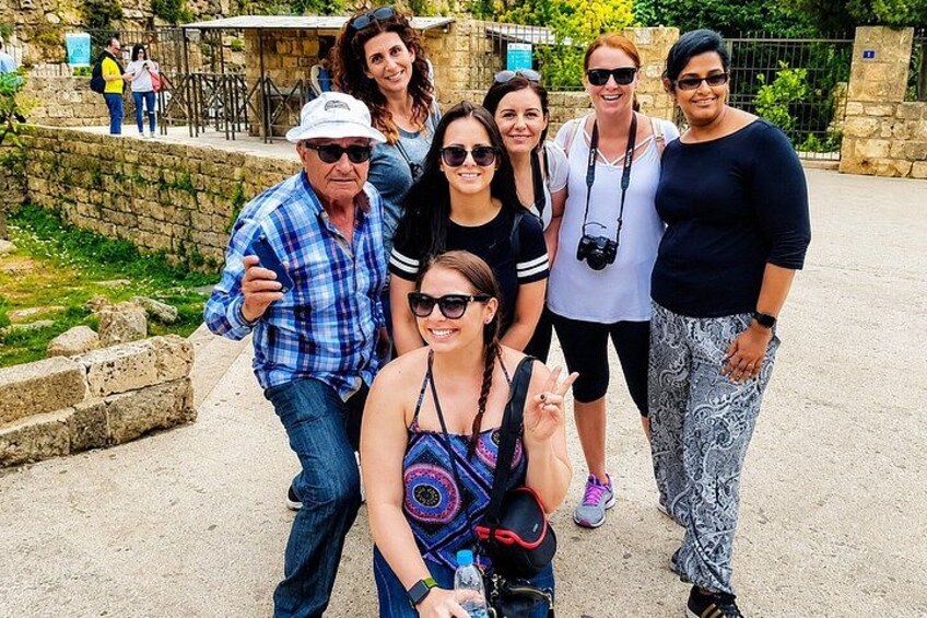 A group of people posing for a photo in an outdoor setting with stone walls and greenery. 3