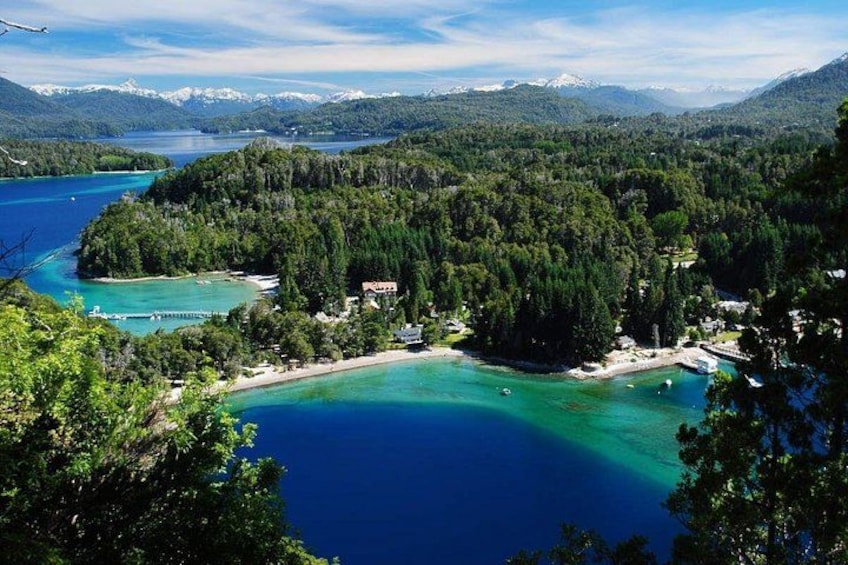 A coastal landscape with a bay, forested hills, and a clear blue sea. 1