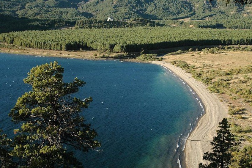 A coastal landscape with a sandy beach, clear blue water, and dense forest in the background. 5
