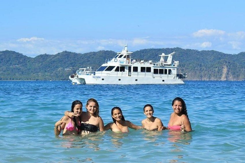 A group of people in a body of water with a large boat in the background. 2