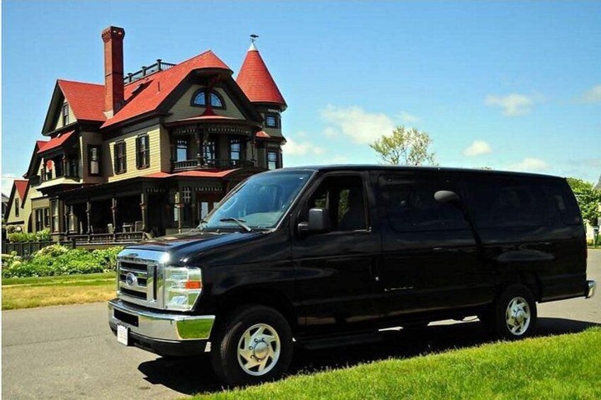 A black van parked in front of a large, historic house with a red roof. 3