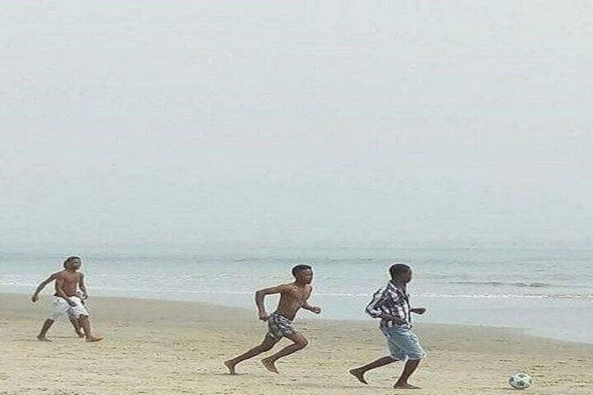 Three children playing soccer on a sandy beach with the ocean in the background. 1