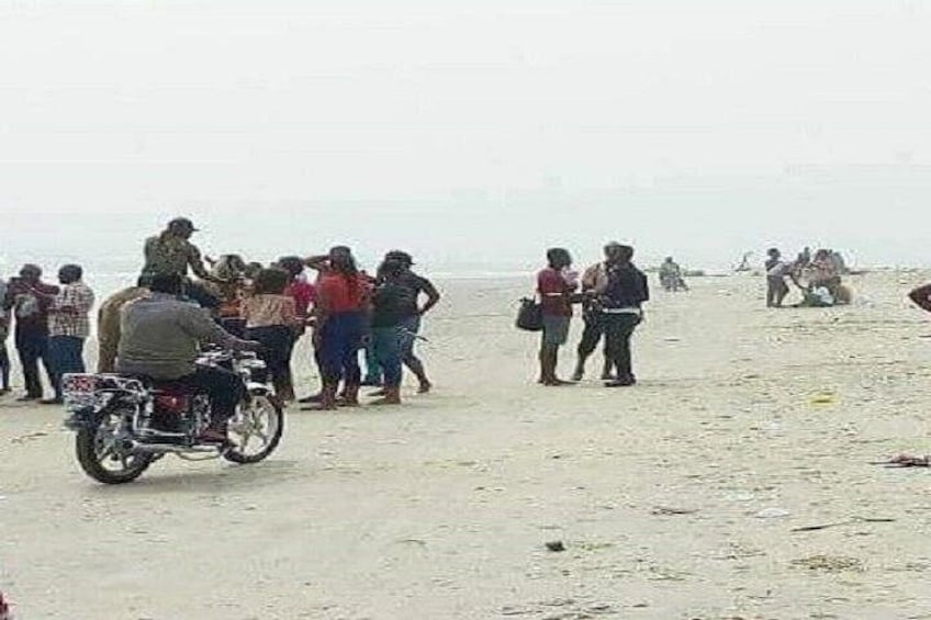 A sandy beach with people gathered, a motorcycle, and a distant shoreline. 3