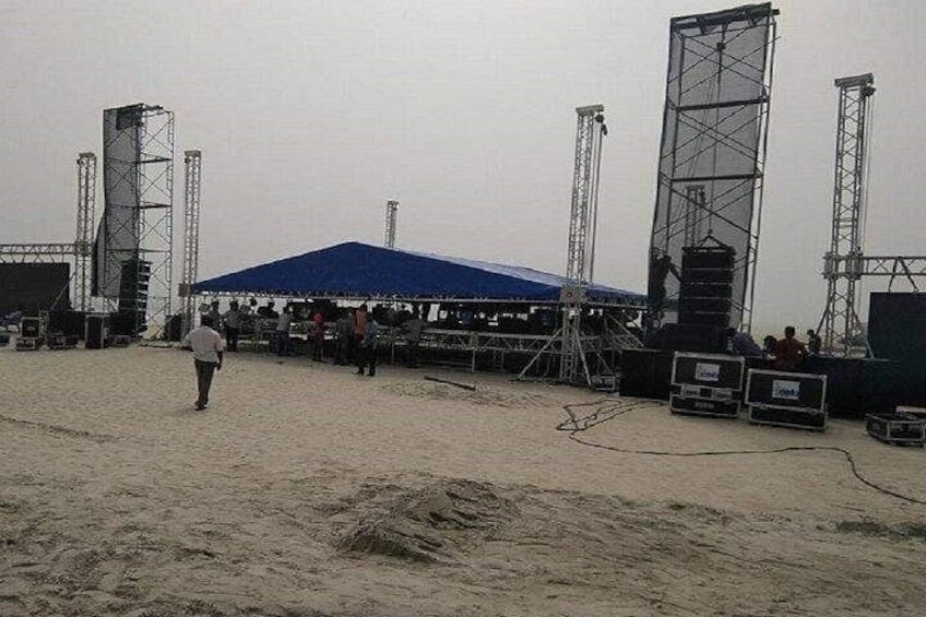 A sandy outdoor area with a blue-roofed structure, metal scaffolding, and a stage. 2