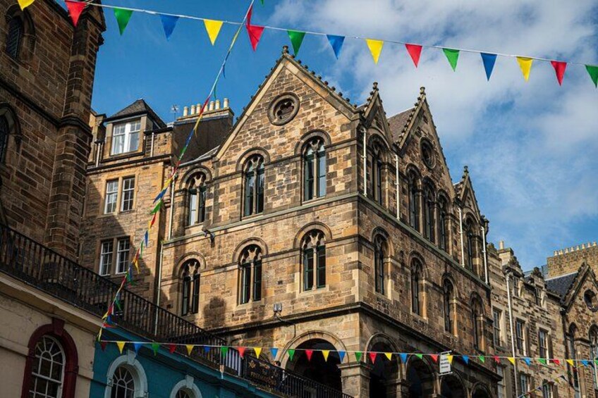 A historic stone building with arched windows and a balcony, decorated with colorful triangular flags. 1