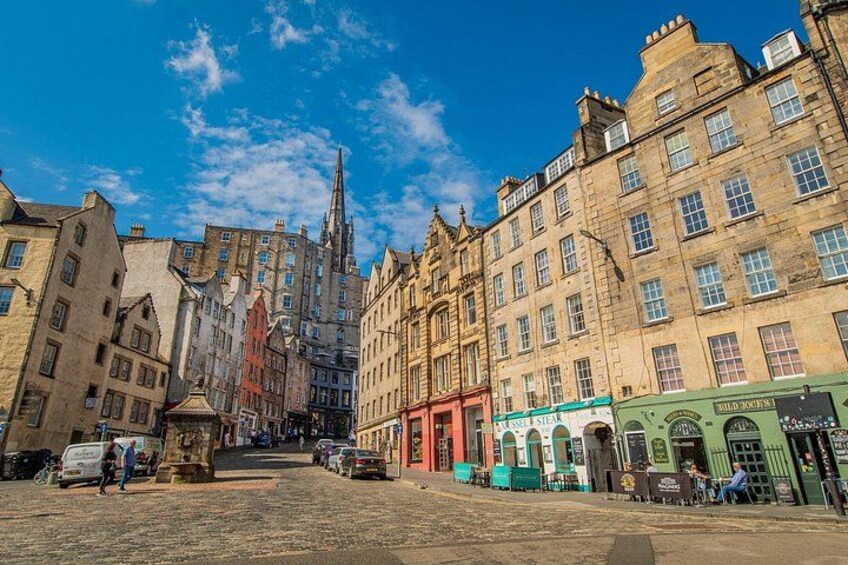 Une rue pavée bordée de bâtiments historiques, avec le clocher d’une église et la façade verdoyante d’un commerce. 4