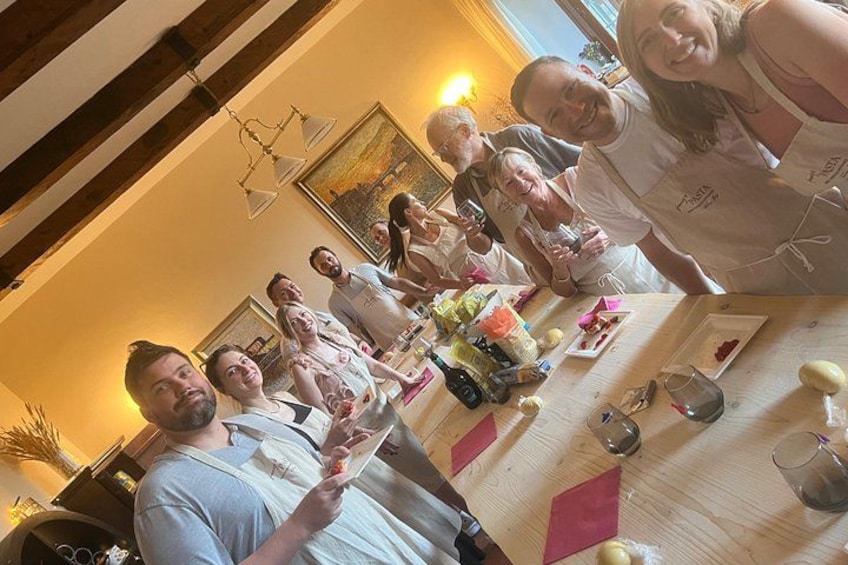 A group of people standing around a table with food and drinks, in a room with wooden beams and a painting on the wall. 4