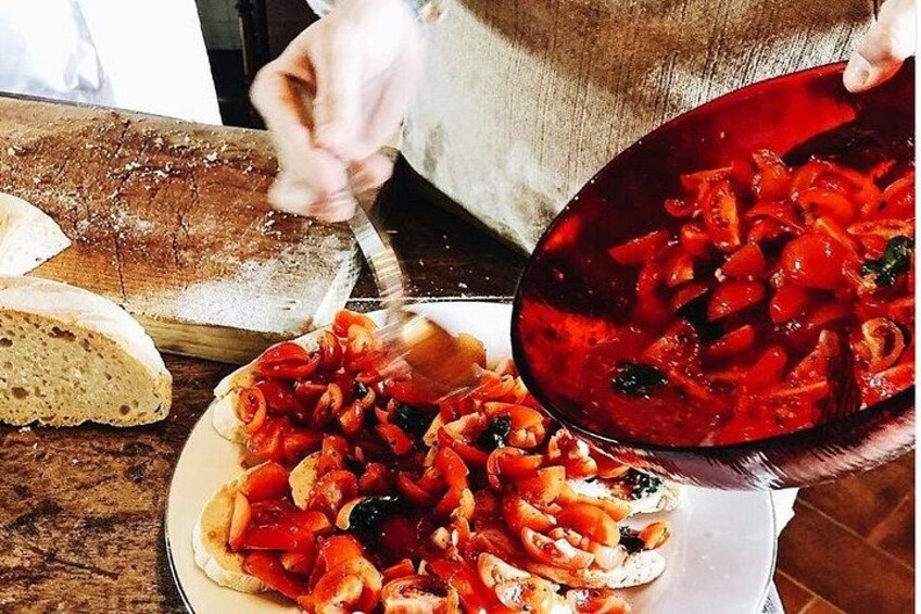 Eine Person bereitet einen Teller mit Tomaten und Oliven zu, im Hintergrund liegt Brot. 2