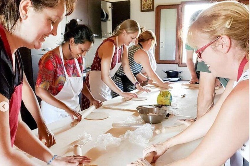 A group of people engaged in a cooking activity, rolling dough on a table. 5