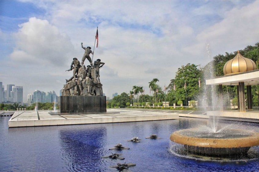 A statue of soldiers on a pedestal, a fountain, and a domed building in a park with a city skyline in the background. 3