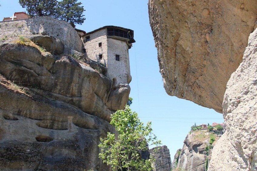 Un edificio in pietra aggrappato a una scogliera rocciosa, circondato da formazioni rocciose naturali. 2