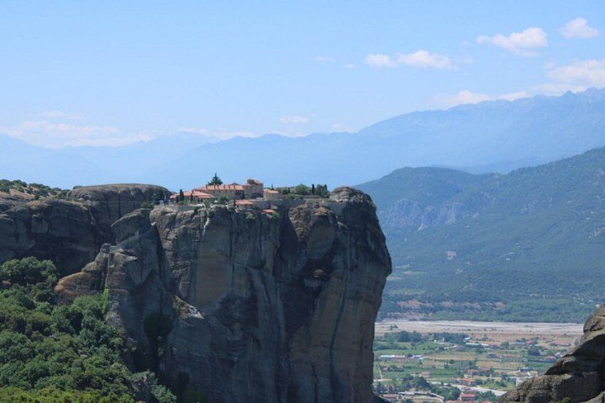 Una scogliera rocciosa con un edificio sulla sommità, circondata da montagne e vegetazione. 3