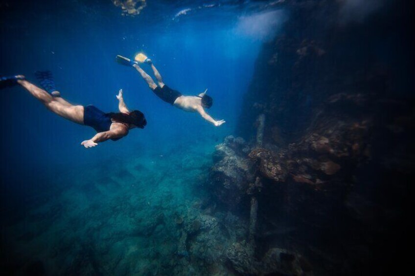 Two people swimming underwater near a rocky structure. 5