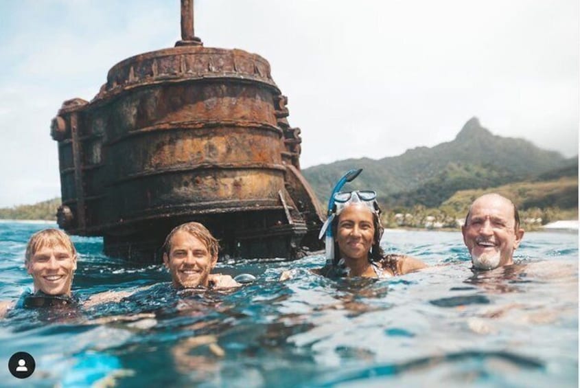 People swimming in water with a rusted shipwreck in the background. 1