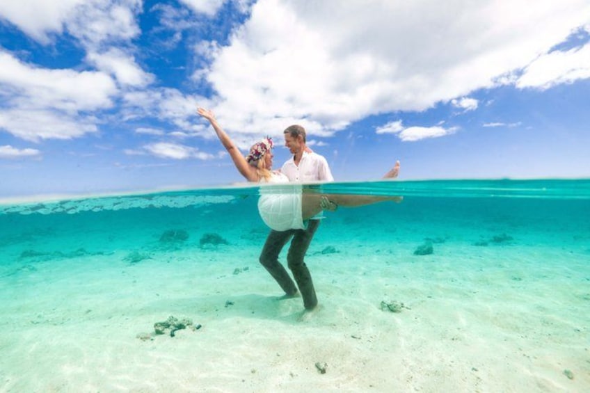 A couple underwater in a clear blue ocean with a sandy bottom and a clear sky above. 2
