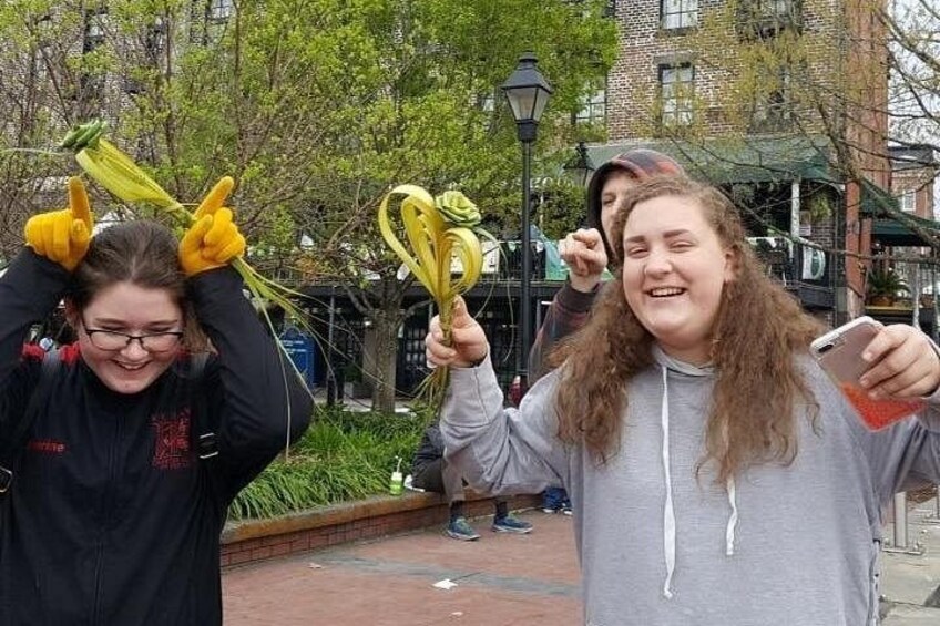 Two people holding yellow flowers in a park with brick buildings in the background. 2