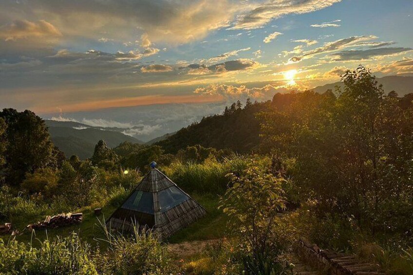 A grassy hill with a small, blue-roofed structure, a sunset, and a forested valley. 1