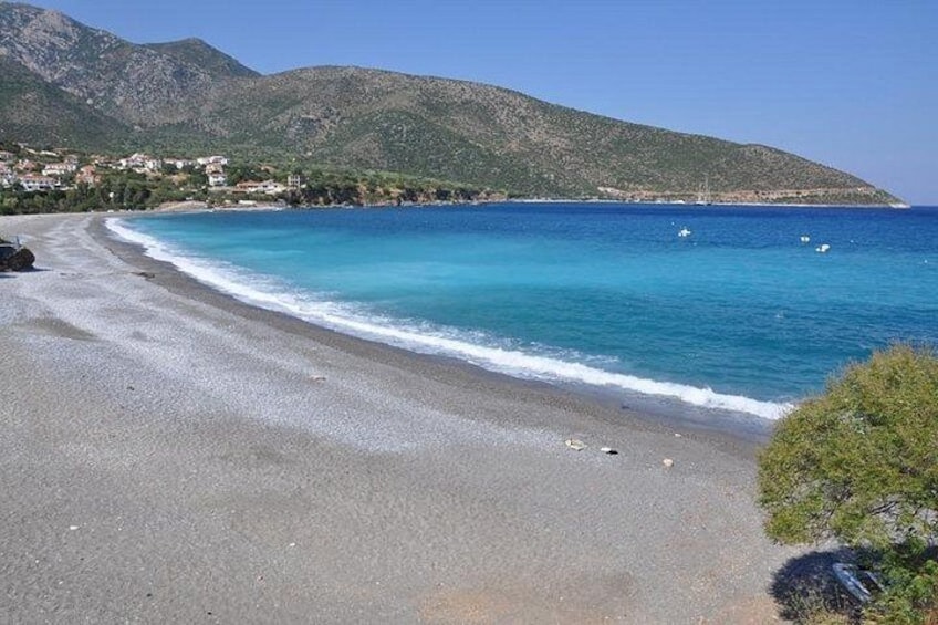 Une plage avec une eau d’un bleu limpide, un rivage sablonneux et une montagne en arrière-plan. 2