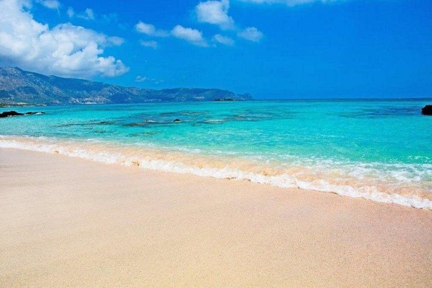 Une plage à l’eau turquoise et limpide, un rivage sablonneux et des montagnes qui se dessinent à l’horizon. 5