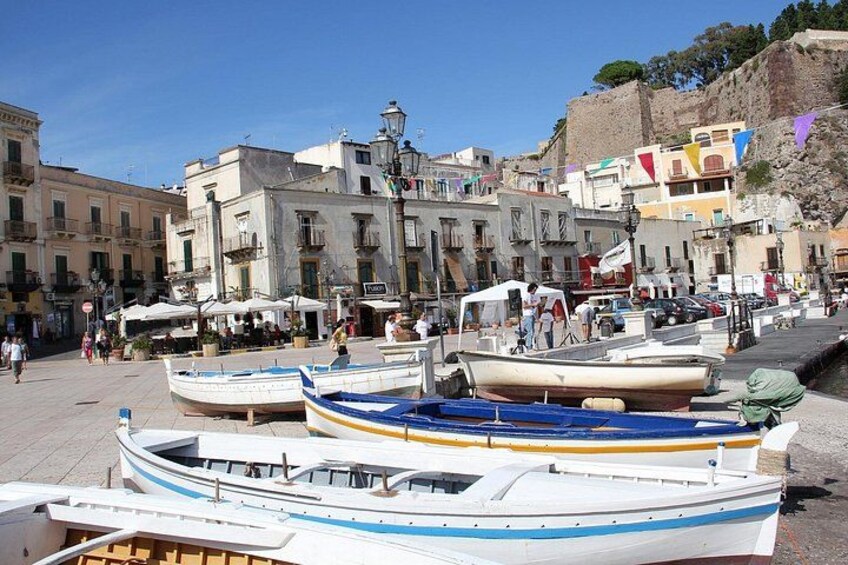 A harbor with boats, buildings, and a rocky hill in the background. 5