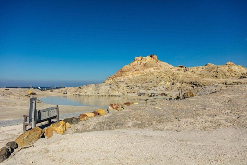 A desert landscape with a rocky hill, a small body of water, and a wooden bench. 2