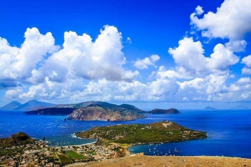 A coastal landscape with a prominent island, clear blue sky, and scattered clouds. 1