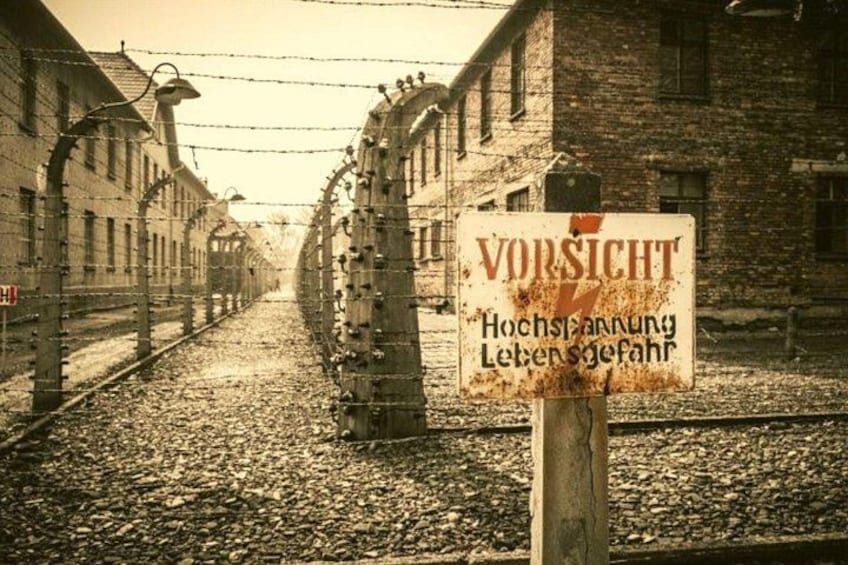 A concentration camp with barbed wire fences, a sign with the word 'VORSICHT' and German text, and a railway track. 2