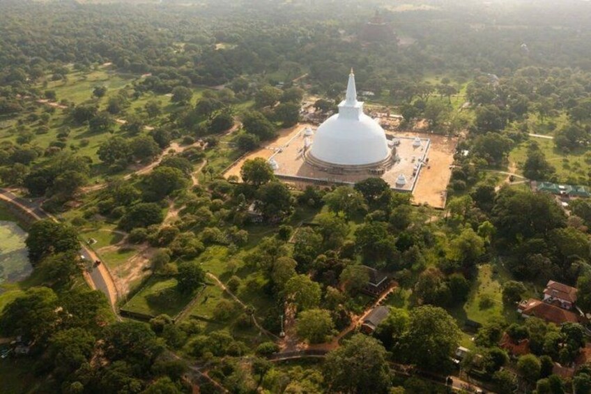 Luchtbeeld van een groot, wit tempel omringd door weelderige begroeiing en enkele verspreide gebouwen. 3