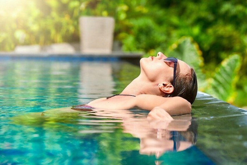 A person relaxing in a clear swimming pool with greenery in the background. 1