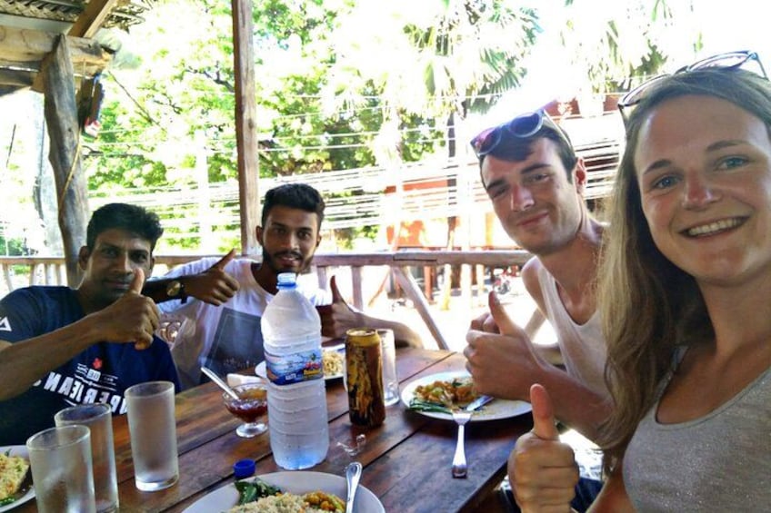 A group of people sitting at a wooden table outdoors, giving thumbs up. 1
