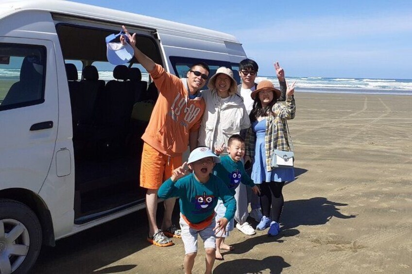 Une famille pose devant un fourgon blanc sur une plage, avec l’océan en arrière-plan. 2