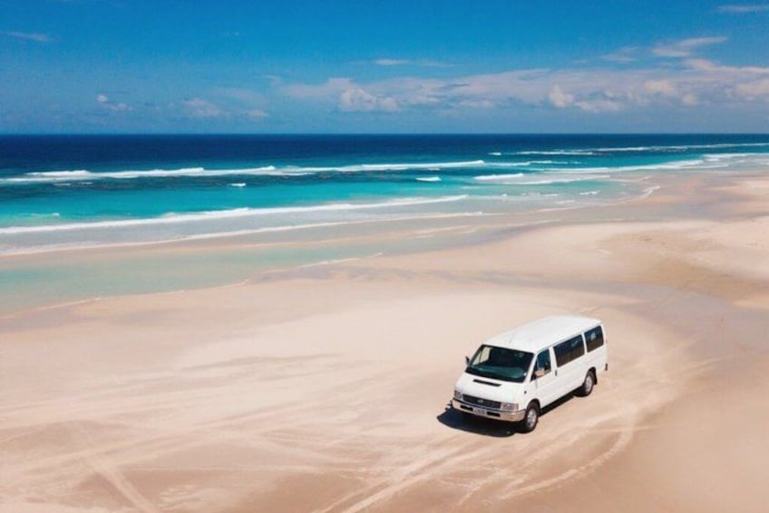 Un fourgon blanc est garé sur une plage de sable, avec l’océan en arrière-plan. 2
