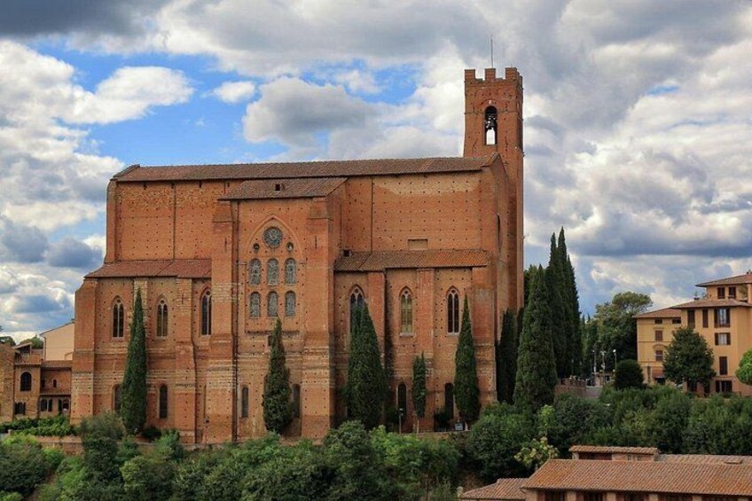 Un edificio grande de ladrillo con una torre, rodeado de vegetación y otros edificios. 3