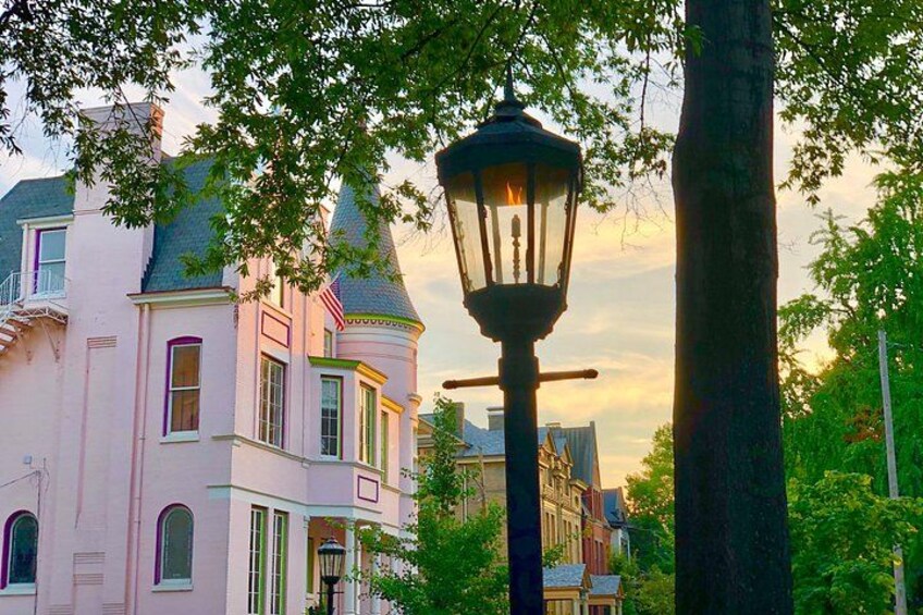 A pink Victorian-style house with a turret, surrounded by trees and a street lamp. 3