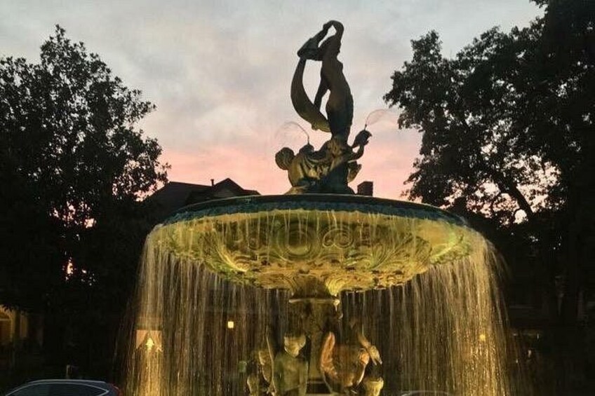 A fountain with a statue of a woman and child, surrounded by trees. 5