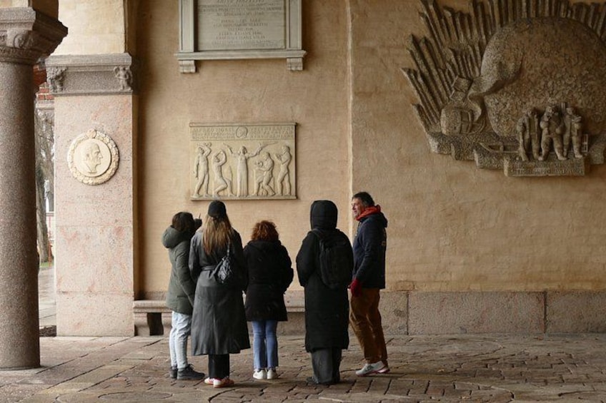 Un groupe de personnes se tient devant un bâtiment orné d’une sculpture en relief et d’une plaque commémorative. 4