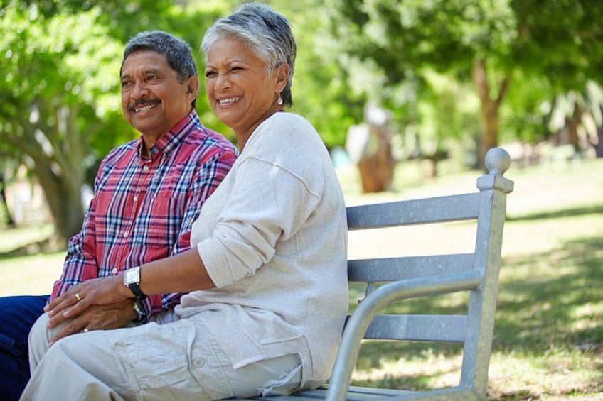 Two people sitting on a bench in a park with trees in the background. 3