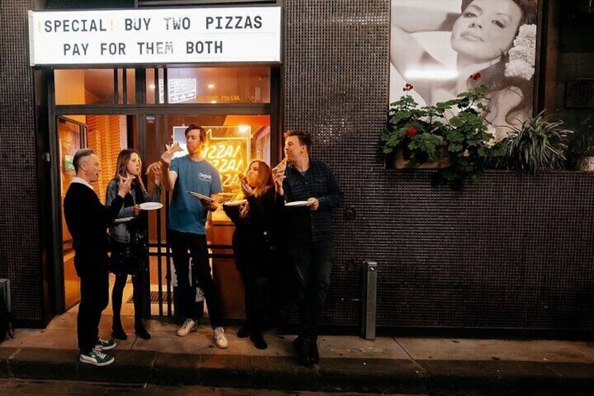 A group of people standing outside a pizza restaurant at night. 3